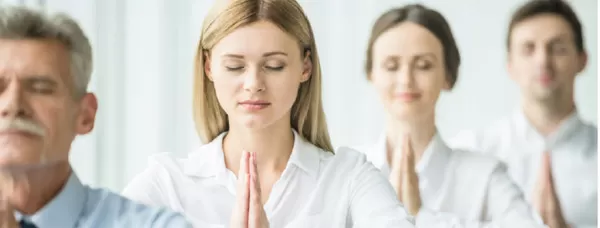 Vier Personen in weißer Arbeitskleidung, die mit geschlossenen Augen und gefalteten Händen meditieren