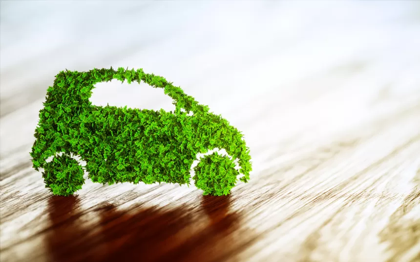 Kleines Auto aus grünem Laub auf hellem Untergrund symbolisiert umweltfreundliche Mobilität