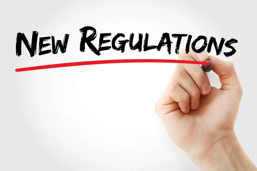 Hand schreibt mit Stift "New Regulations" an eine Glasscheibe