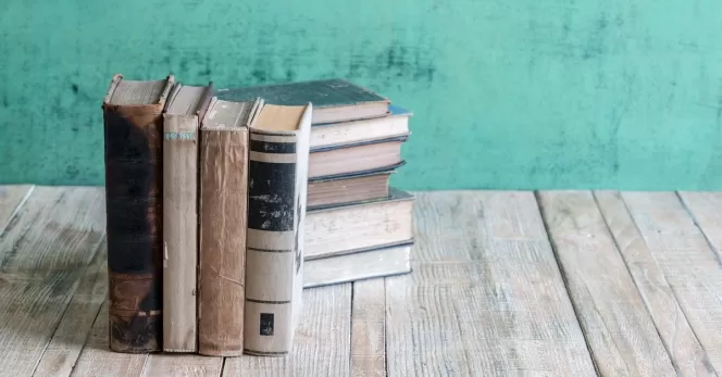 Mehrere alte Bücher stehen auf einem Holztisch vor einer türkisfarbenen Wand