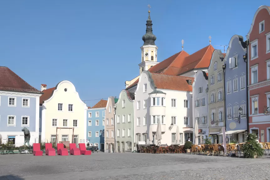 Historische Gebäude mit bunten Fassaden und einem Kirchturm im Hintergrund an einem sonnigen Marktplatz