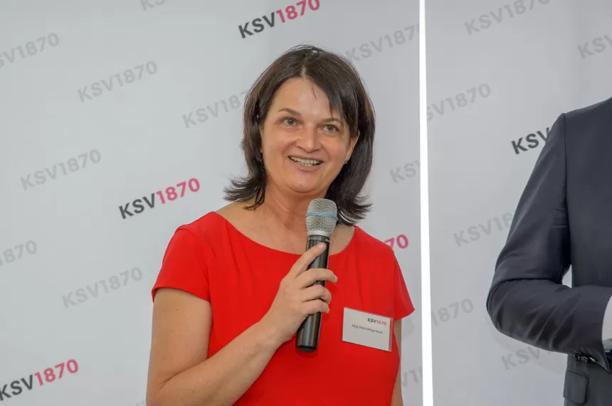 Frau mit braunen Haaren trägt rotes Oberteil und hält Mikrofon vor KSV1870-Hintergrund