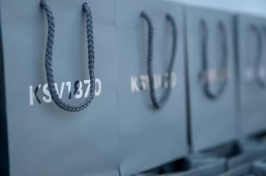 Mehrere graue Einkaufstaschen mit schwarzen Griffen und der Aufschrift 'KSV1870' nebeneinander