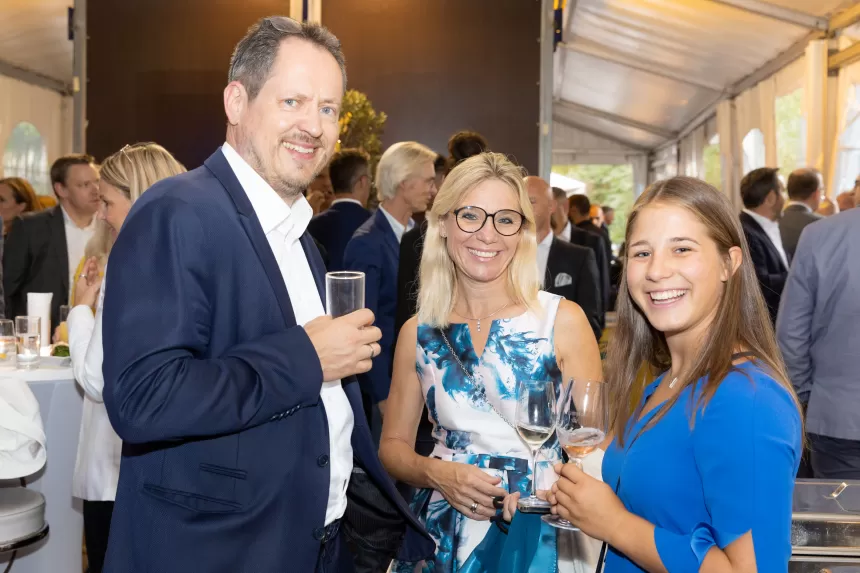 Drei Personen in eleganter Kleidung unterhalten sich mit Getränken beim Sommerausklang des KSV1870 in einem Festzelt