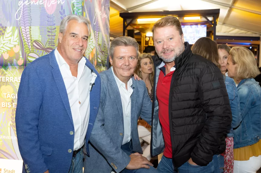 Drei Männer in Jacken und Hemden stehen zusammen bei Sommerausklang des KSV1870 in einem belebten Innenraum