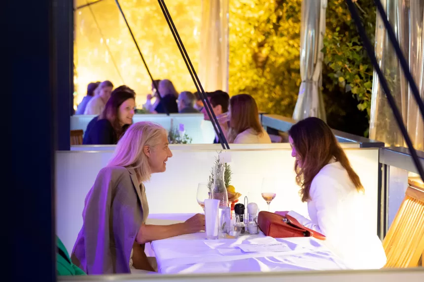 Zwei Frauen sitzen an einem gedeckten Tisch bei der Abendveranstaltung Sommerausklang des KSV1870, umgeben von weiteren Gästen in einem beleuchteten Außenbereich