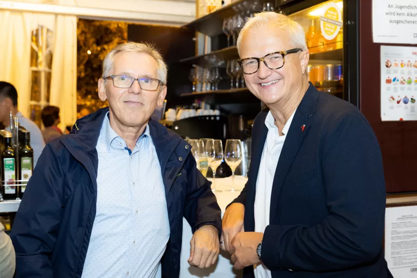 Zwei Männer in Anzügen stehen vor einer Bar beim Sommerausklang des KSV1870 und lächeln in die Kamera