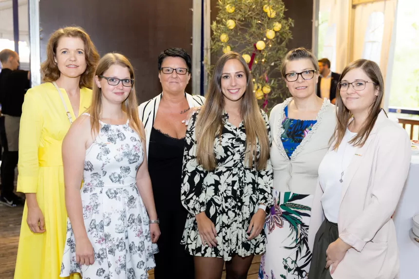 Sechs Frauen in formeller Kleidung stehen nebeneinander und lächeln in die Kamera