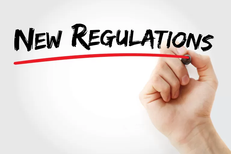 Hand schreibt mit Stift "New Regulations" an eine Glasscheibe