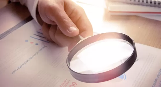 Hand hält Lupe über Diagramm mit Datenpunkten und Linien