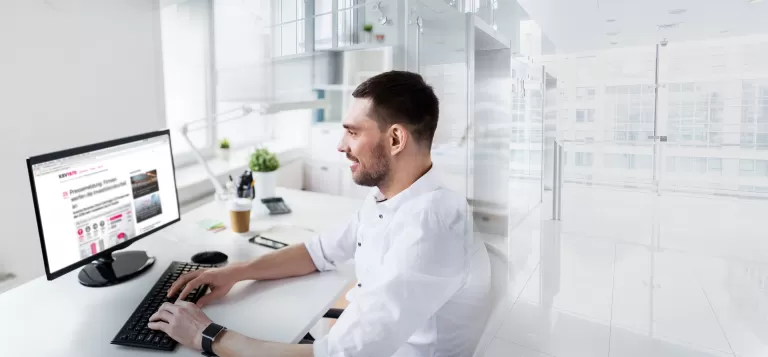 Mann sitzt an einem Schreibtisch und arbeitet an einem Computer mit mehreren Bildschirmen in einem modernen Büro