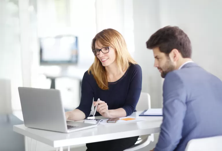 Zwei Personen sitzen an einem Tisch und arbeiten gemeinsam an einem Laptop in einem modernen Büro