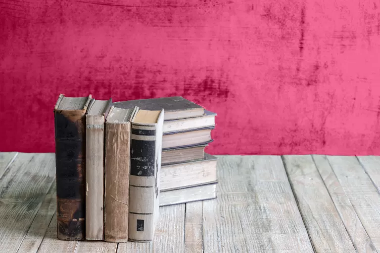 Mehrere alte Bücher stehen auf einem Holztisch vor einer roten Wand