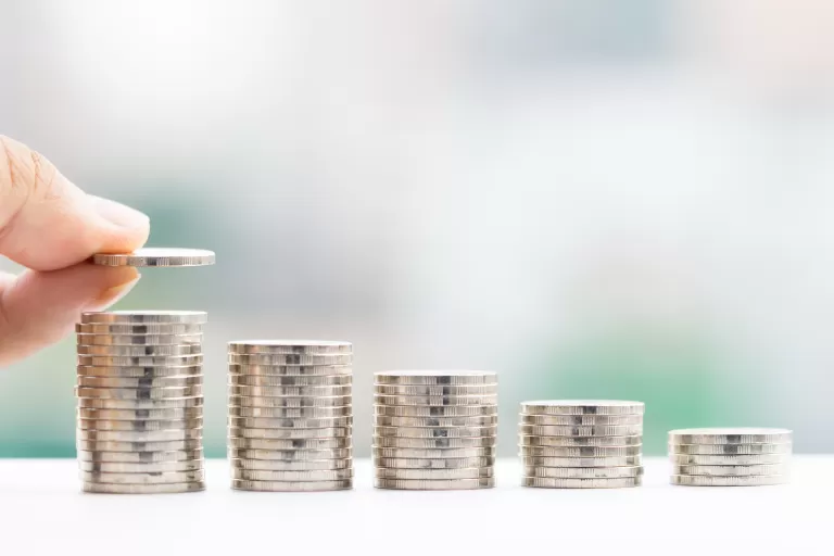 Hand legt Münze auf den höchsten von fünf Münzstapeln, die von links nach rechts abnehmen