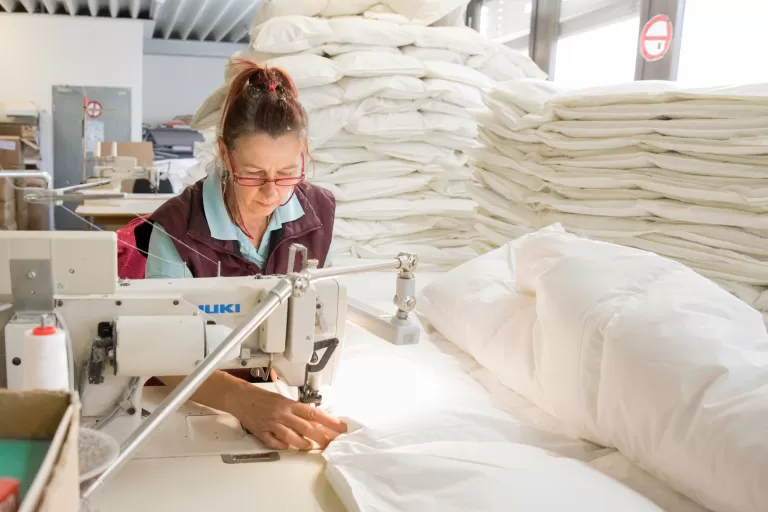Person näht mit einer Industrienähmaschine große weiße Stoffstücke in einer hellen Werkstatt