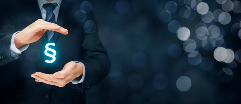 Geschäftsmann hält leuchtendes Paragraphenzeichen zwischen den Händen vor dunklem Hintergrund