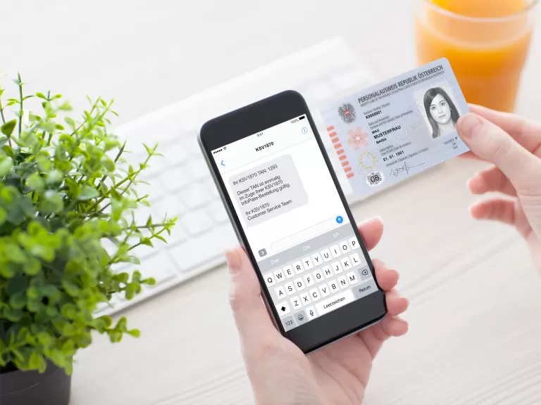 Hand hält Personalausweis und Smartphone mit geöffneter Textnachricht zur Selbstauskunft