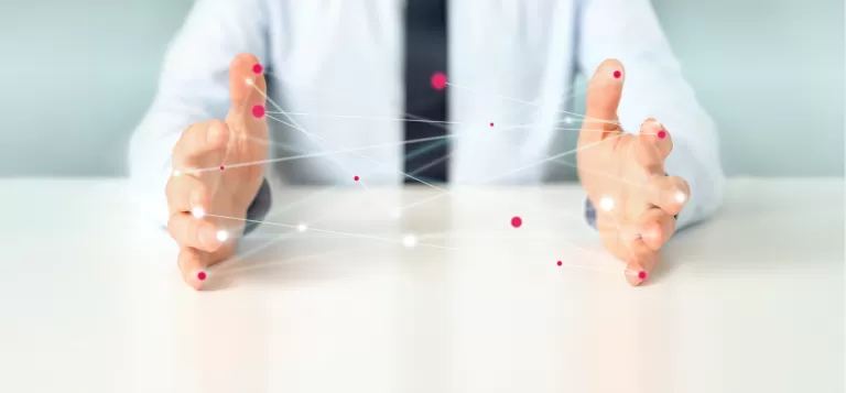 Zwei Hände eines Menschen in weißem Hemd, die sich über einem weißen Tisch befinden und ein Netz mit bunten Kungeln aufgespannt haben