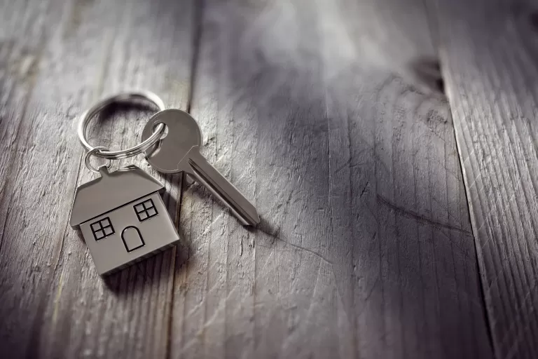 Hausschlüssel mit Schlüsselanhänger in Form eines Hauses auf Holzoberfläche