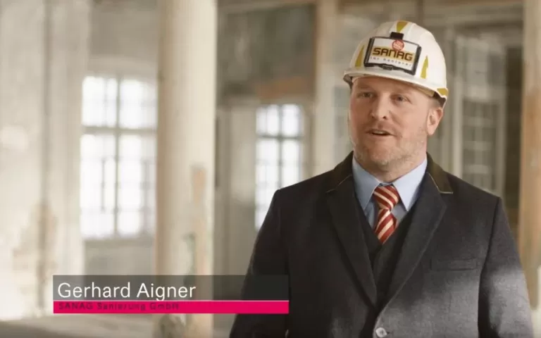 Gerhard Aigner trägt einen Anzug mit Hemd und gestreifter Krawatte in einem historischen Gebäude