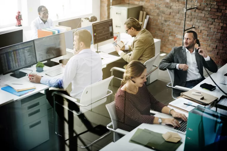 Büro mit vielfältigen Fachkräften, die an Schreibtischen mit Computern arbeiten, Gespräche führen und telefonieren.