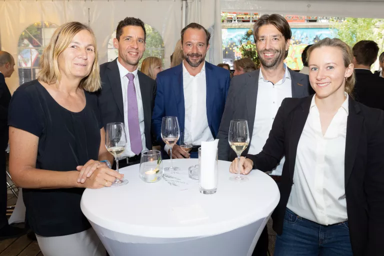 Fünf Personen stehen um einen Stehtisch mit weißen Tischdecke, halten Weingläser beim Sommerausklang des KSV1870