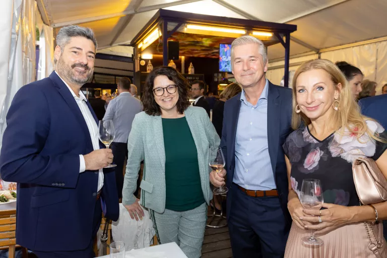 Vier Personen in einem Zelt beim Sommerausklang des KSV1870, zwei halten Weingläser, Hintergrund mit weiteren Gästen und Barbereich