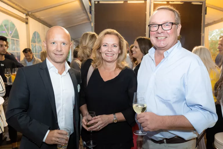 Drei Personen beim Sommerausklang des KSV1870, zwei Männer und eine Frau, stehend mit Getränken in der Hand in einem festlich beleuchteten Zelt