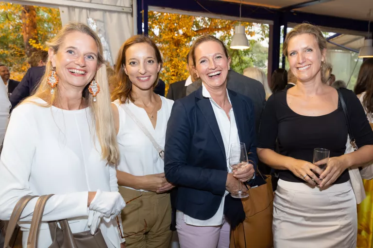 Vier Frauen beim Sommerausklang des KSV1870, stehend in einem hellen Raum mit großen Fenstern, tragen elegante Freizeitkleidung