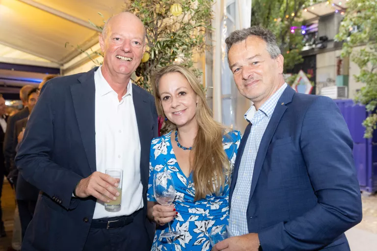 Drei Personen in eleganter Kleidung beim Sommerausklang des KSV1870, zwei Männer in Anzügen und eine Frau im blauen Kleid, halten Getränke