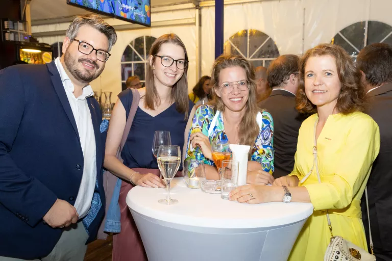 Vier Personen stehen um einen Stehtisch mit Getränken beim Sommerausklang des KSV1870 in einem Zelt mit anderen Gästen im Hintergrund