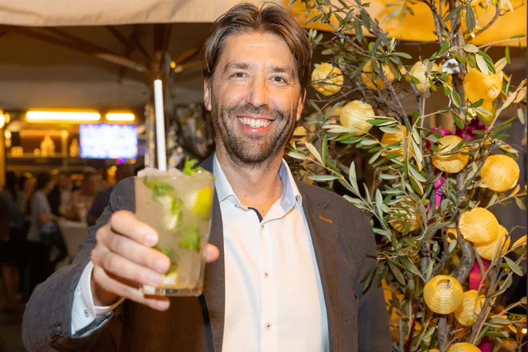 Mann in weißem Hemd und dunklem Sakko hält Cocktailglas mit Limettenscheiben und Minze bei Sommerausklang des KSV1870