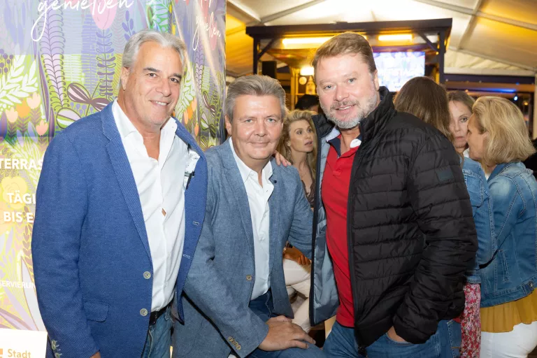 Drei Männer in Jacken und Hemden stehen zusammen bei Sommerausklang des KSV1870 in einem belebten Innenraum