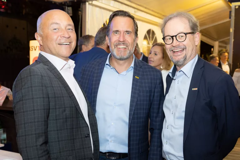 Drei Männer in Anzügen stehen zusammen beim Sommerausklang des KSV1870 in einem festlich beleuchteten Zelt