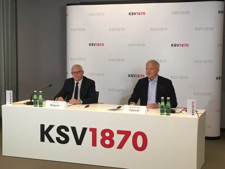 Zwei Männer im Anzug, Gerhard Wagner und Ricardo-José Vybiral, sitzen hinter einem Tisch mit dem Schriftzug 'KSV1870' und geben ein Interview