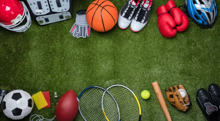 Unterschiedliche Sportartikel auf Grass. Zum Beispiel: Boxhandschuhe, Helm, Baseballschläger, Tennisball, Fußball, Handschuhe und mehr.