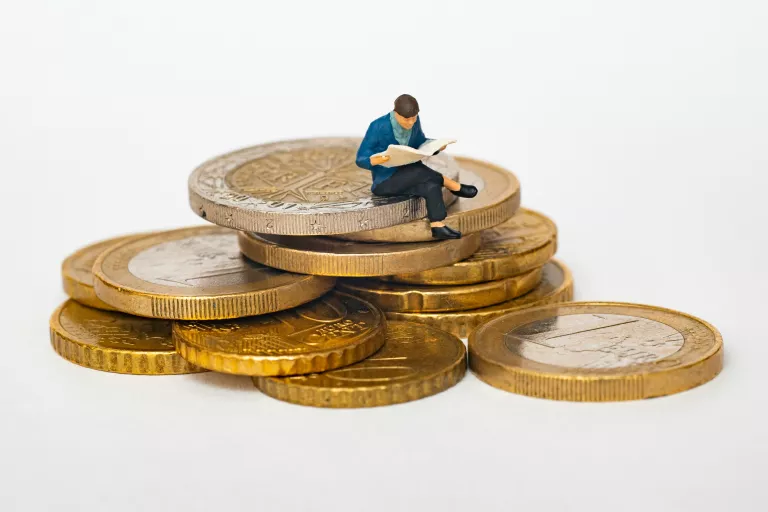 Winzige Figur sitzt auf ein paar Euromünzen und schaut betrübt - "auf dem Geld sitzen bleiben"