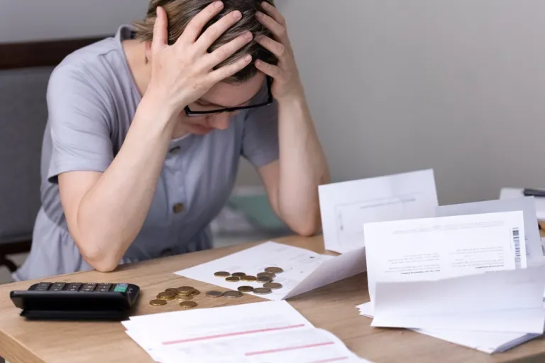 Frau umgeben von Quittungen, Münzen und einem Taschenrechner, greift sich auf den Kopf