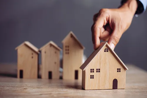 Hand berührt ein Mini-Holz-Haus-Figur
