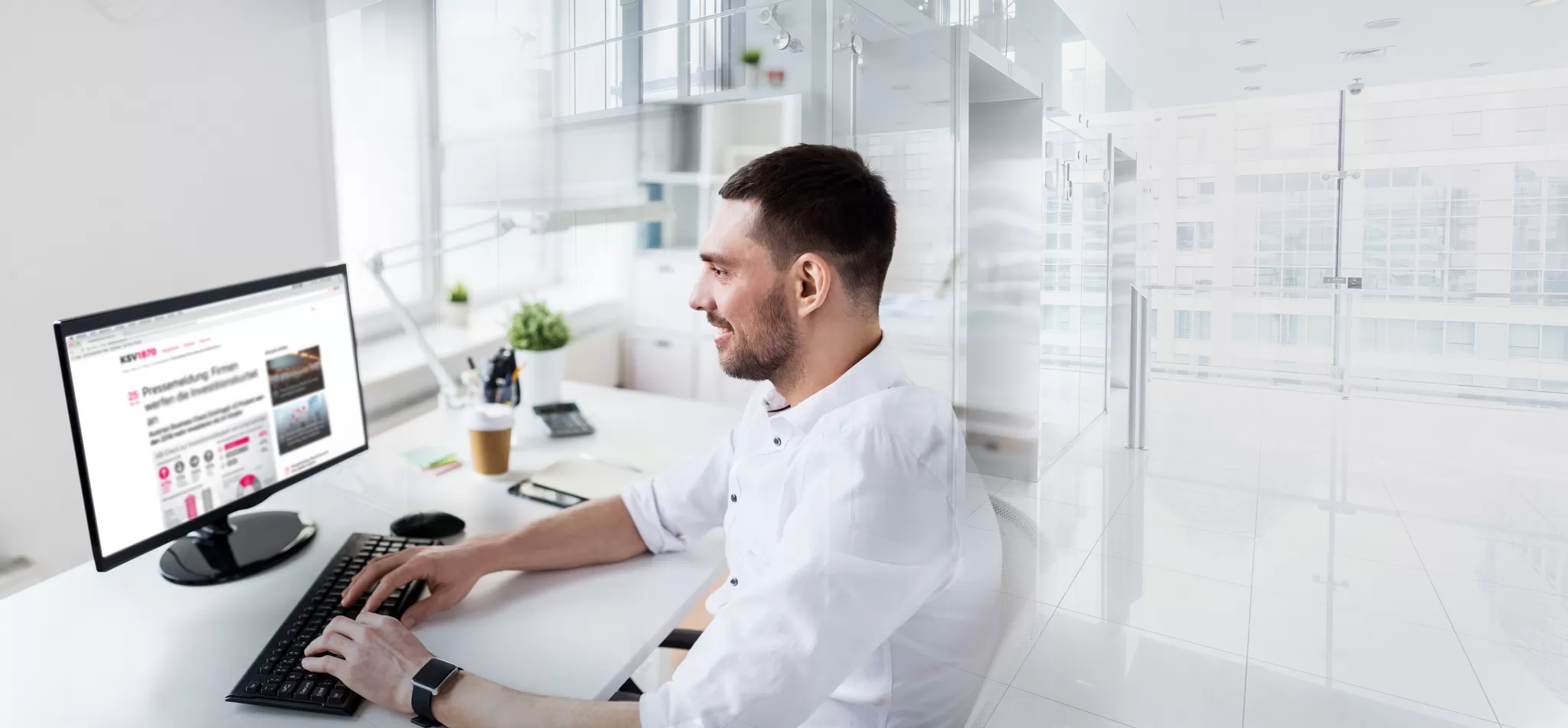 Mann sitzt an einem Schreibtisch und arbeitet an einem Computer mit mehreren Bildschirmen in einem modernen Büro