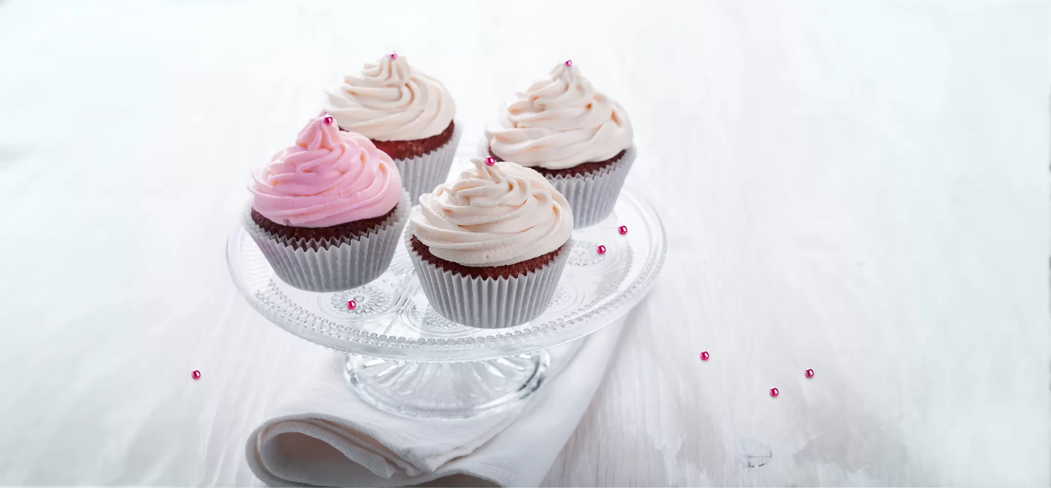 Vier Schokoladen-Cupcakes mit rosa und weißem Zuckerguss auf einem Glasständer
