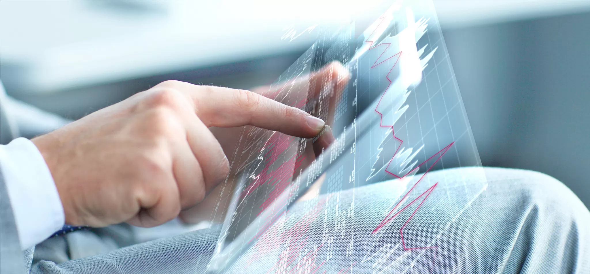 Hand tippt auf Tablet mit Finanzdiagrammen im Vordergrund