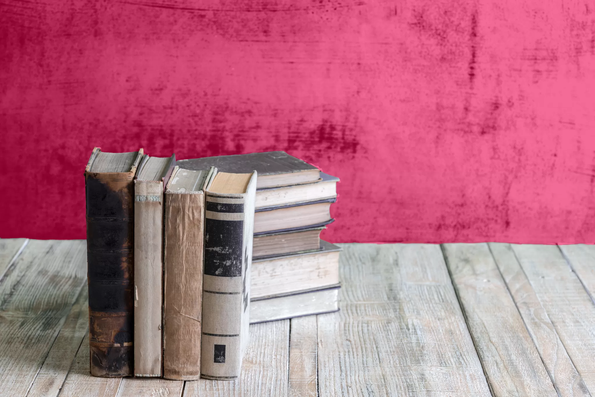 Mehrere alte Bücher stehen auf einem Holztisch vor einer roten Wand