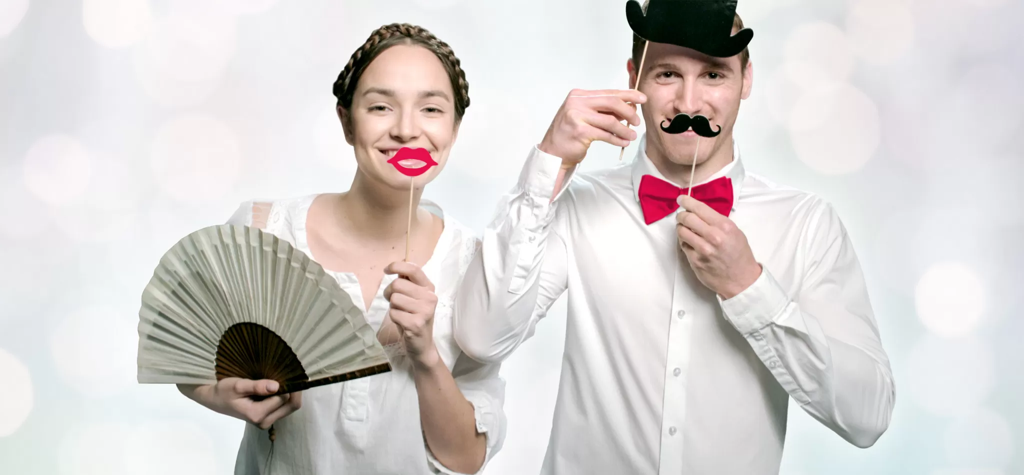 Ein Mann und eine Frau in historischen Kostümen, der Mann mit Schnurrbart und roter Fliege, die Frau mit Fächer und rotem Lippenstift