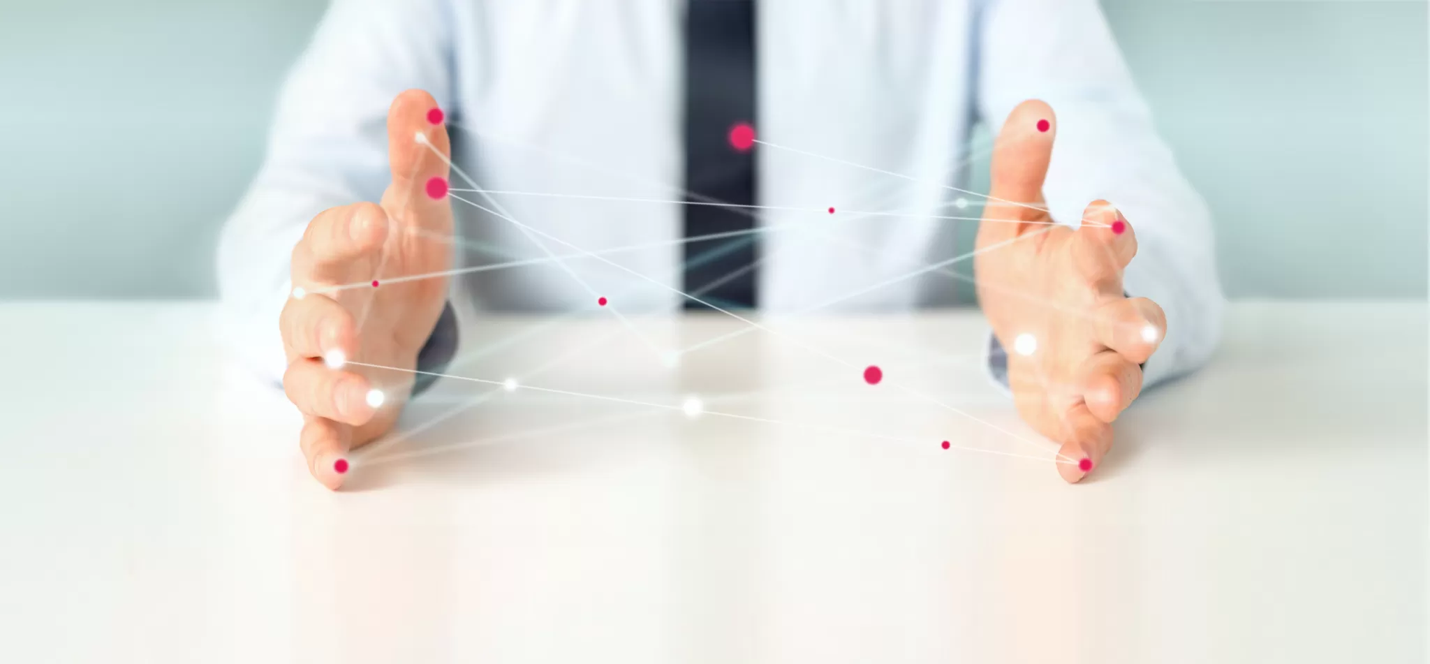 Zwei Hände eines Menschen in weißem Hemd, die sich über einem weißen Tisch befinden und ein Netz mit bunten Kungeln aufgespannt haben