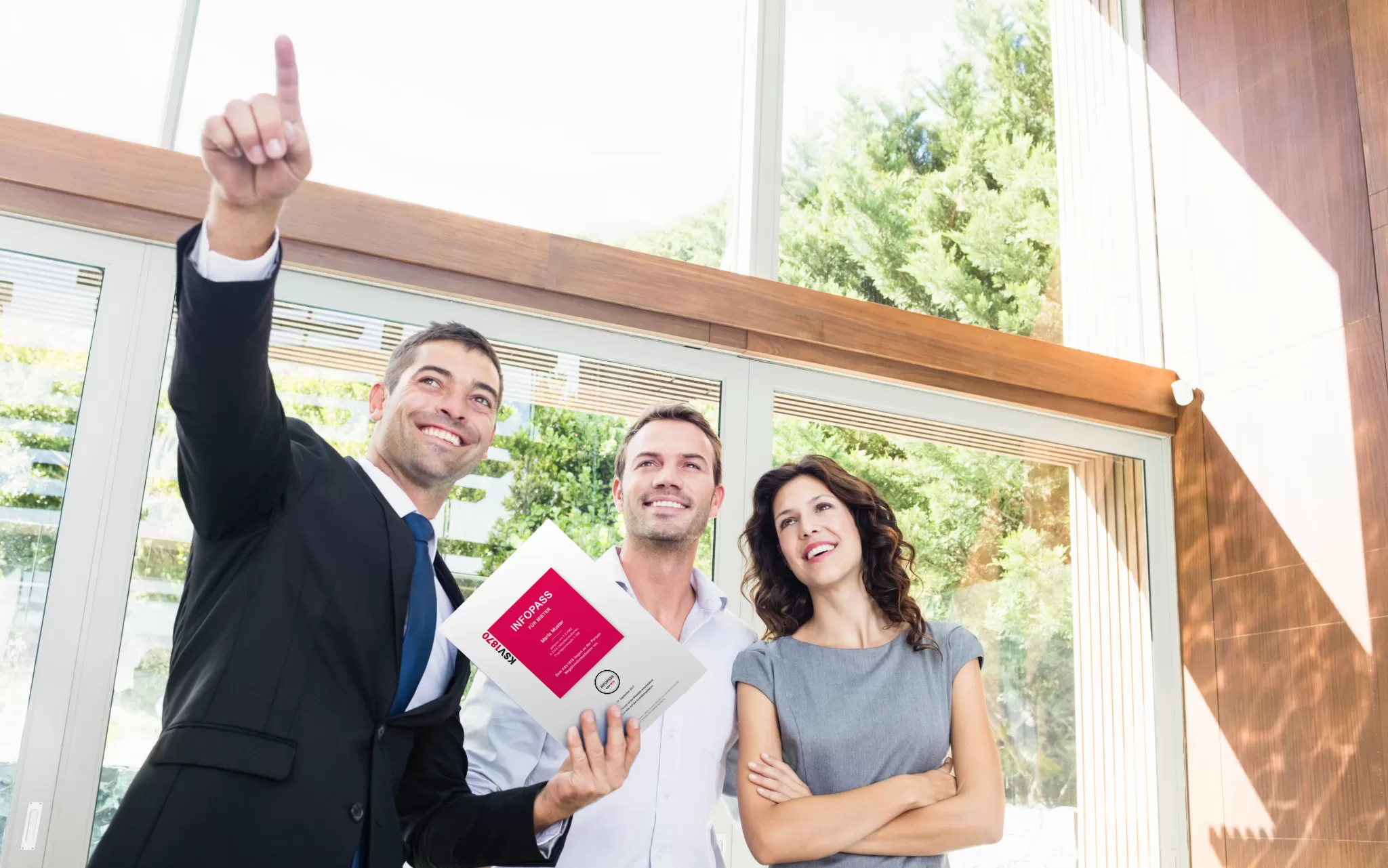 Drei Personen in einem modernen Raum, eine Person zeigt mit dem Finger nach oben, eine hält einen InfoPass, eine dritte Person steht mit verschränkten Armen