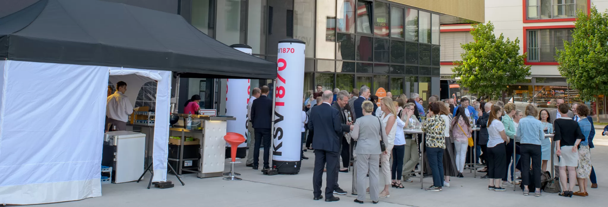 Eröffnungsfeier des neuen Büros in Linz: Menschen versammeln sich vor einem modernen Bürogebäude mit gelber Fassade und Glasvordach