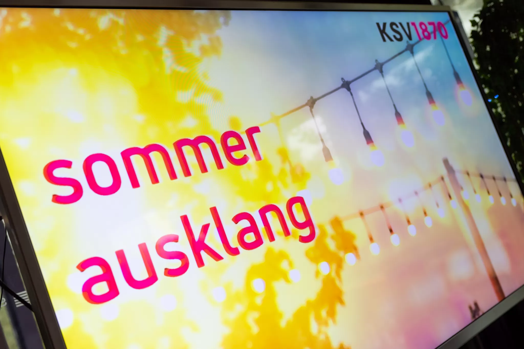 Leuchtreklame mit dem Text 'sommer ausklang' vor einem Hintergrund mit Lichterketten und Sonnenlicht