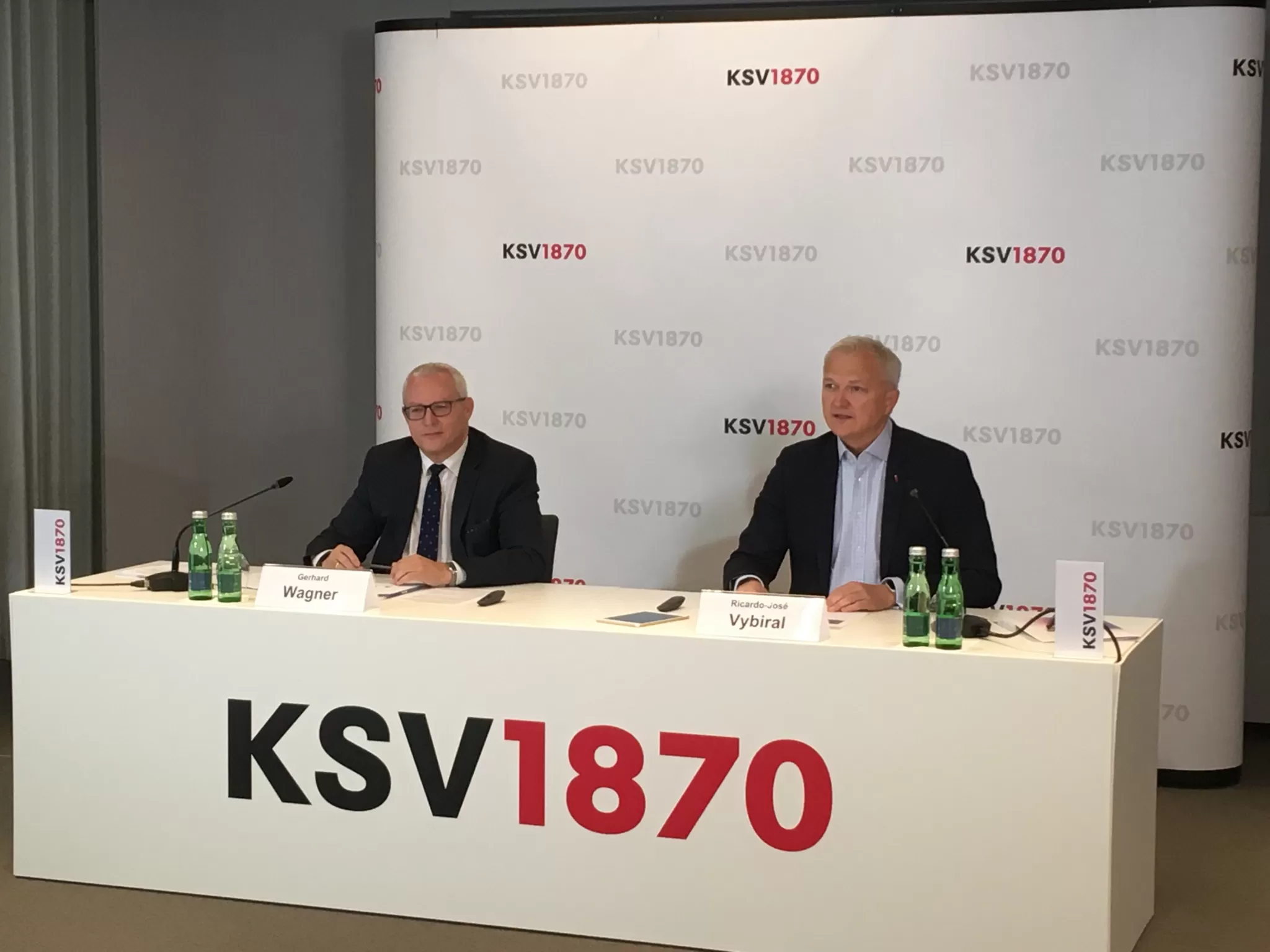 Zwei Männer im Anzug, Gerhard Wagner und Ricardo-José Vybiral, sitzen hinter einem Tisch mit dem Schriftzug 'KSV1870' und geben ein Interview